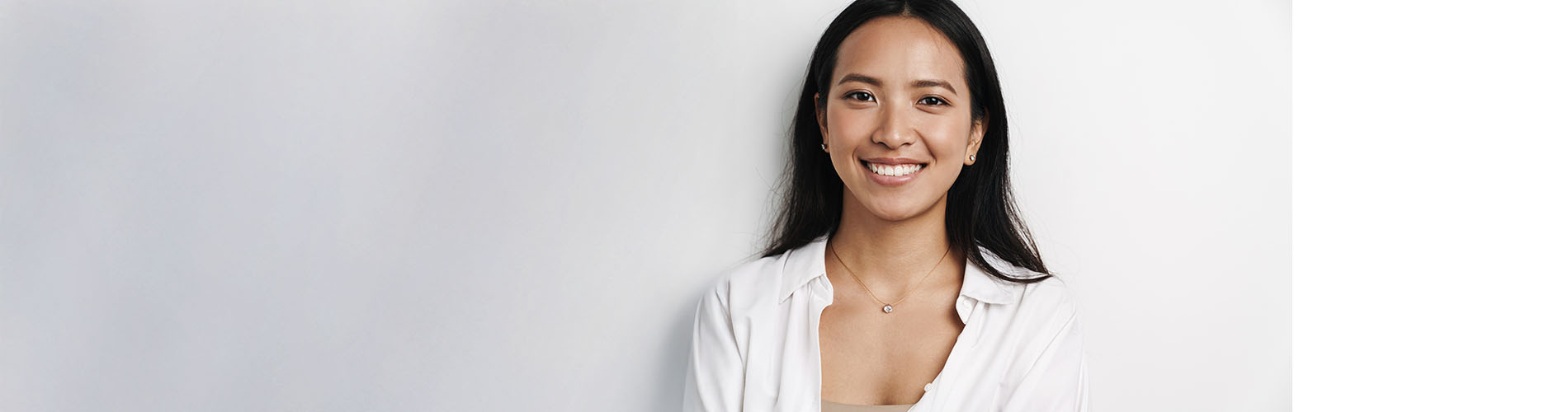 The image is a photograph of a woman with light skin, smiling at the camera. She appears to be in her late twenties or early thirties and has long hair. Her eyes are looking directly at the camera, and she is holding up her index finger near her mouth as if she s making a point or emphasizing something. The background is plain and light-colored, which suggests that this could be a stock photo used for various purposes such as advertising, personal branding, or lifestyle content.
